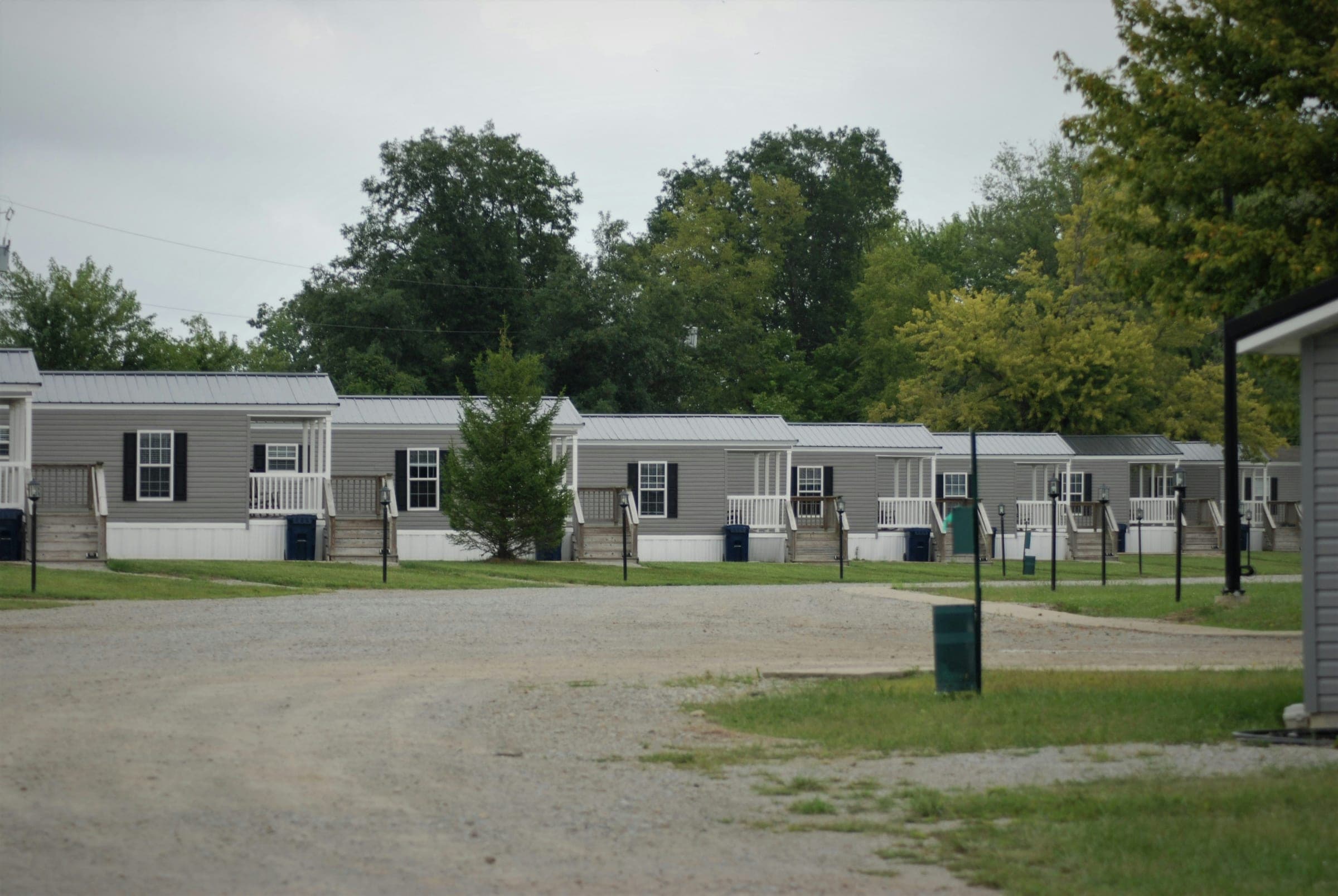A row of manufactured homes with covered porches, set back from a gravel drive.
